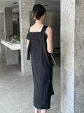 Woman in a black dress standing in a modern indoor setting with concrete walls.