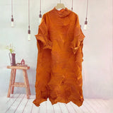 Orange textured dress hanging on a hanger against a light gray wall with a wooden stool and plant in the background.