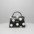 Black handbag with white polka dots on a light surface.