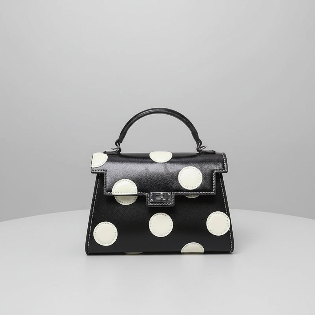 Black handbag with white polka dots on a light surface.