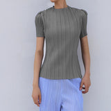 Person wearing a green pleated top and light blue pants against a plain background