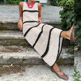 Person wearing a long, sleeveless, white dress with black stripes sitting on stone steps.