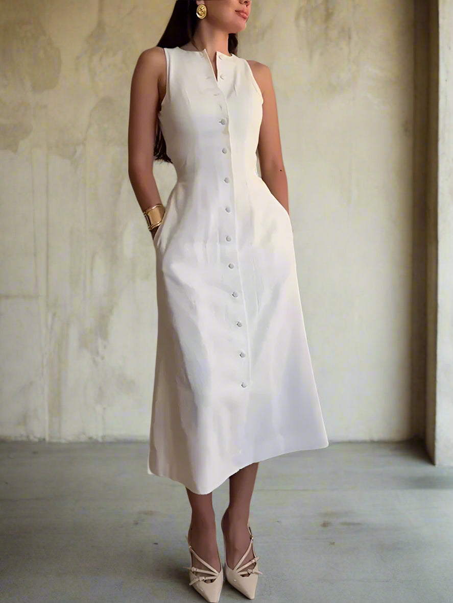 Woman wearing a white sleeveless dress with buttons against a neutral wall.