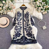 White dress with black floral embroidery on a gray surface with flowers and a hat in the background