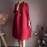 Person wearing a red dress standing against a plain wall with decorative plants.