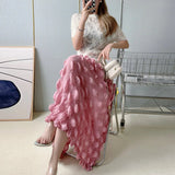 Woman sitting on a chair wearing a white lace top and pink ruffled skirt.