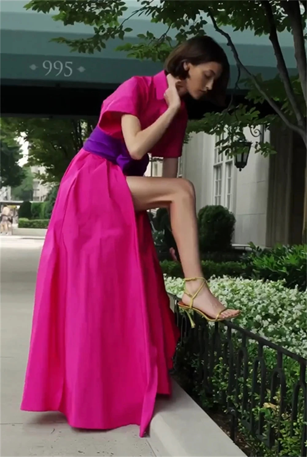 Woman in a bright pink dress sitting on a railing outdoors.