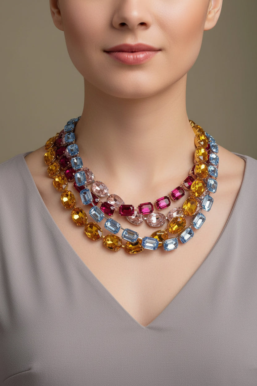 A multi-strand statement necklace featuring faceted gemstones in yellow, light blue, pink, and dark red, displayed on a gray velvet jewelry bust.