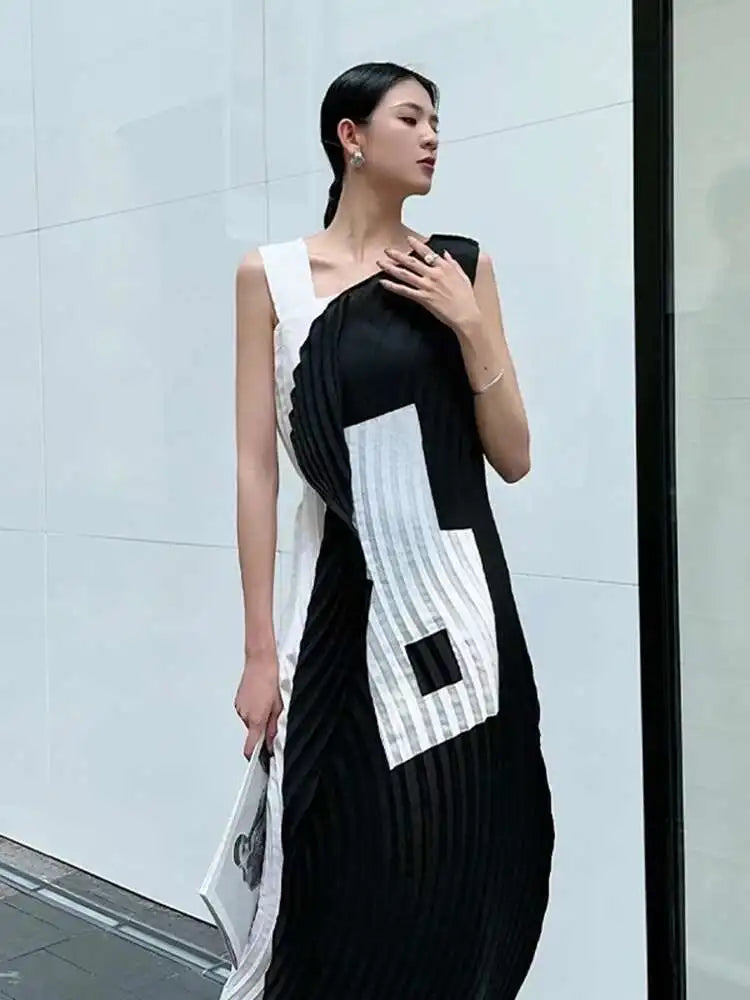 Woman wearing a black and white dress with geometric patterns against a light gray wall.