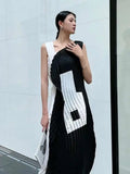 Woman wearing a black and white dress with geometric patterns against a light gray wall.