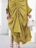 Person wearing a mustard yellow dress with a white handbag on a light background