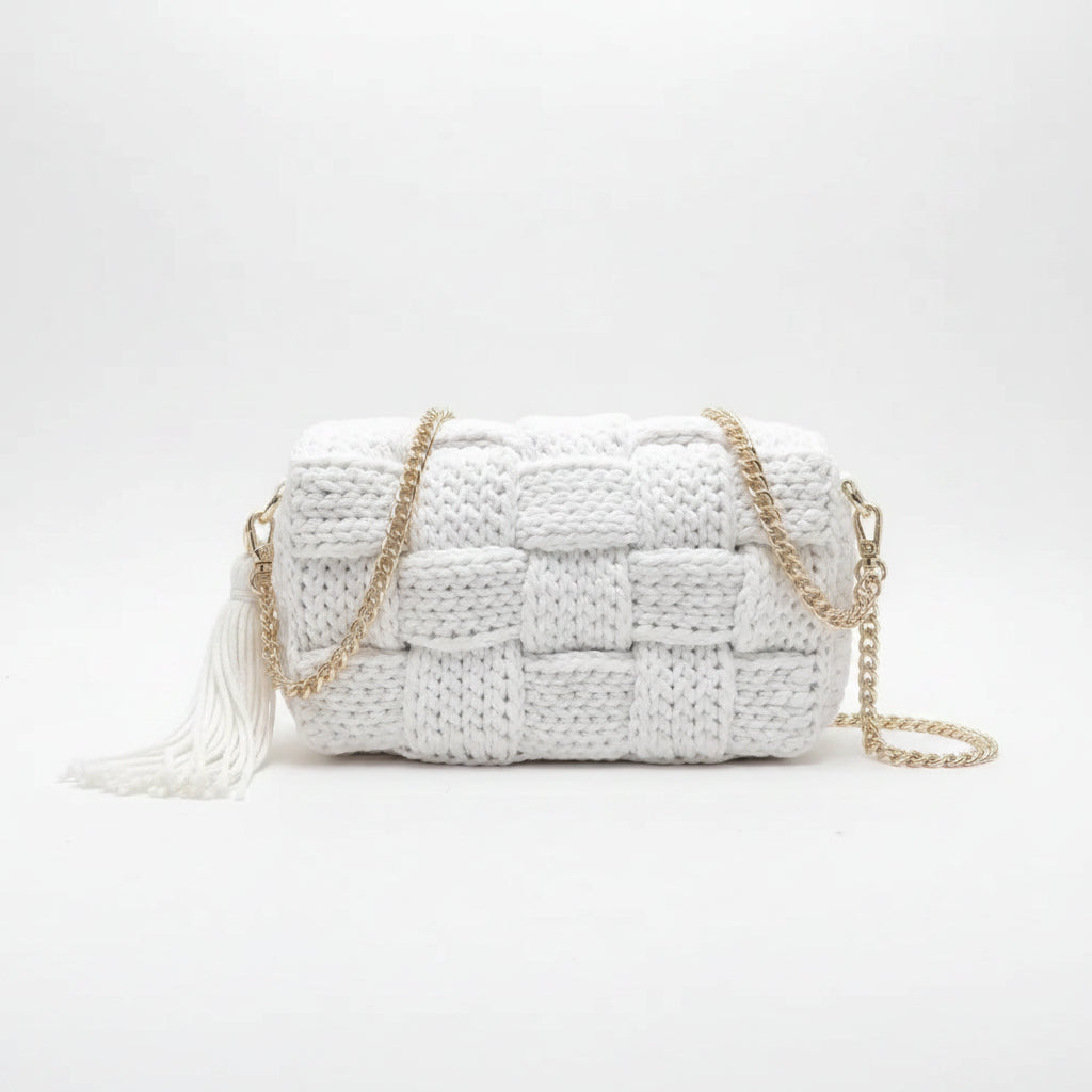 White woven handbag with gold chain strap on a soft fabric background