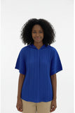 Person wearing a blue pleated dress with a colorful geometric-patterned bag, standing in front of a clothing rack.