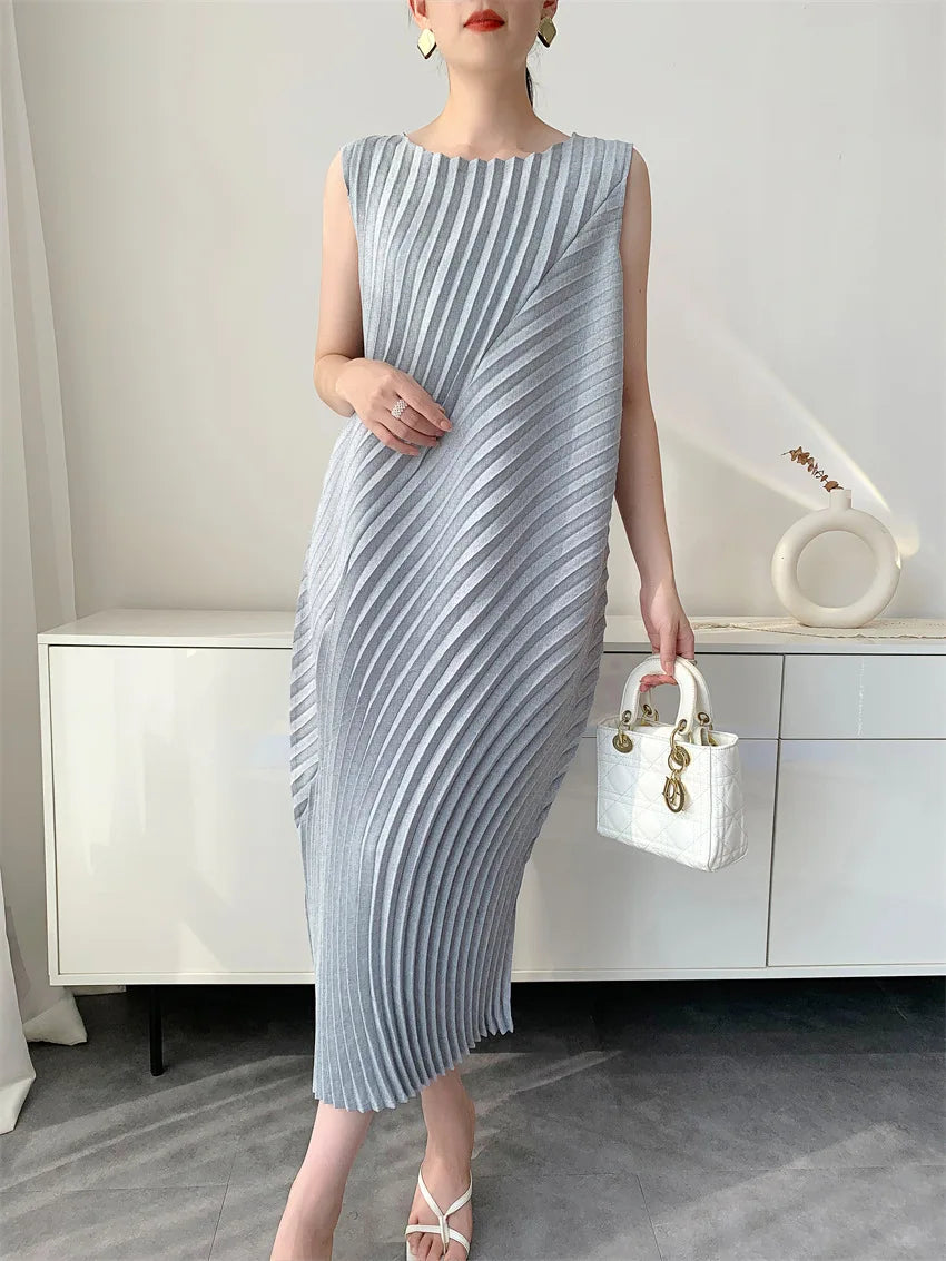 Woman wearing a gray pleated dress holding a white handbag in an indoor setting.