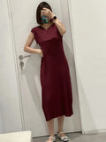 Person wearing a maroon dress standing against a white door.