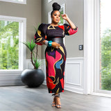 Woman in a colorful dress standing in a modern room with large windows.
