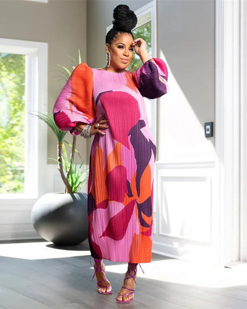Woman in a colorful dress standing in a bright room with large windows.