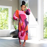 Woman in a colorful dress standing in a bright room with large windows.