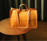 Brown leather tote bag on a wooden table with a dark curtain background
