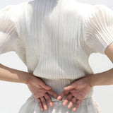 Person wearing a white ribbed knit top on a plain background