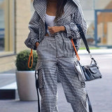 Person wearing a black and white checkered outfit with a handbag on a city street.
