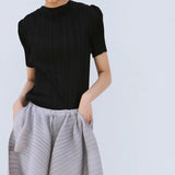 Person wearing a black top and gray pleated skirt on a light blue background