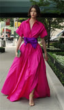 Woman in a bright pink dress with a purple belt walking on a sidewalk.