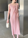 Woman wearing a pink pleated dress holding a white clutch in an indoor setting.
