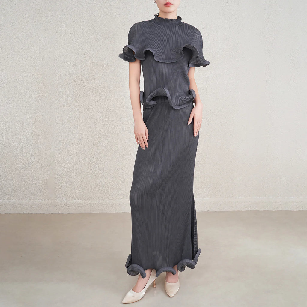 Woman wearing a long dark gray dress with ruffled top on a plain background