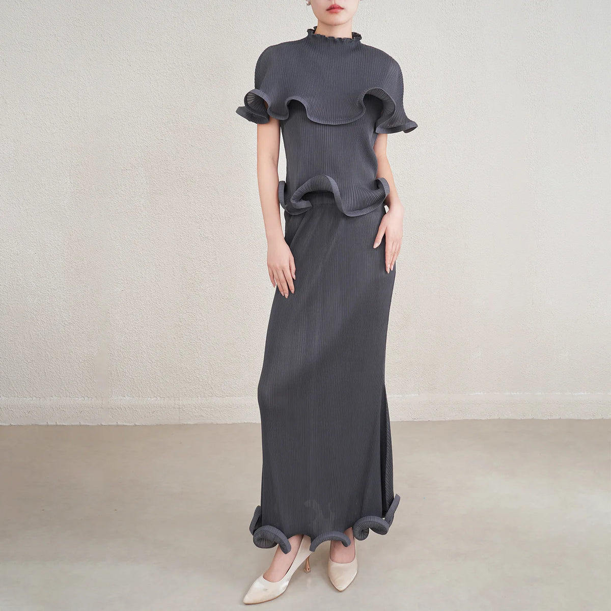 Woman wearing a long dark gray dress with ruffled top on a plain background
