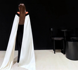 Person wearing a black dress with a white cape in a minimalistic setting.