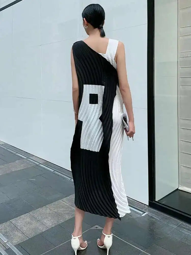 Woman wearing a black and white dress standing against a light gray wall.