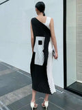 Woman wearing a black and white dress standing against a light gray wall.