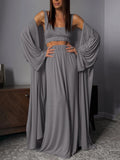 Woman wearing a gray dress with flowing sleeves in a room.