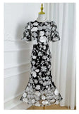 Black dress with white floral embroidery on a mannequin against a white curtain background