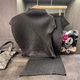 Dark gray pleated skirt on a hanger with a handbag and colorful knitted items in the background.