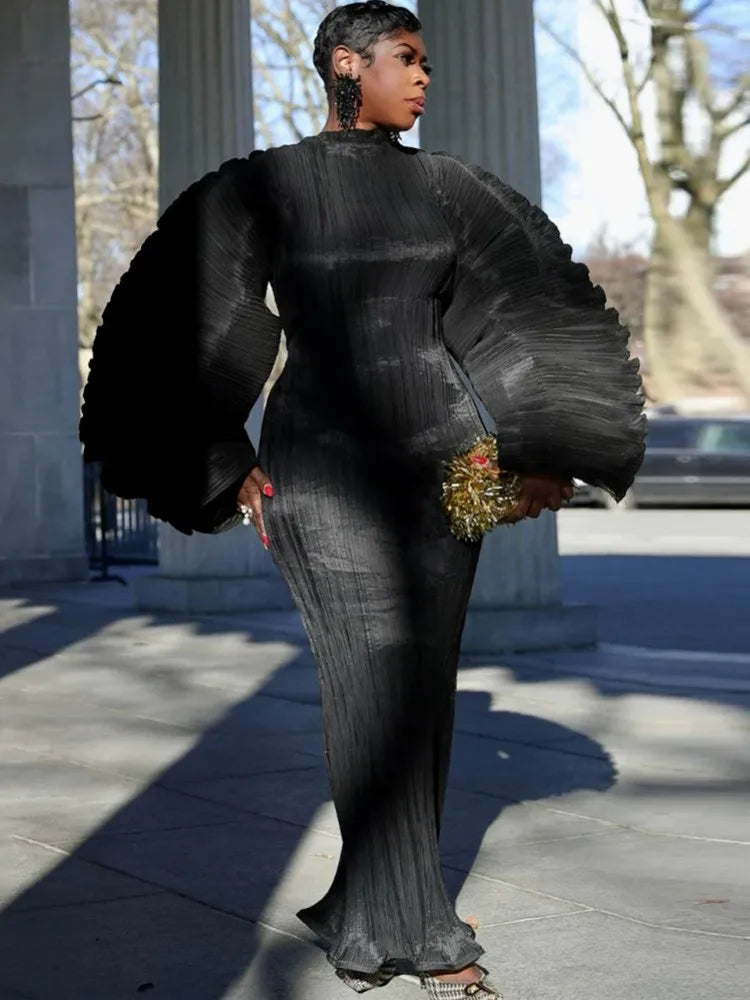 Person wearing a black outfit with large sleeves in an outdoor setting.