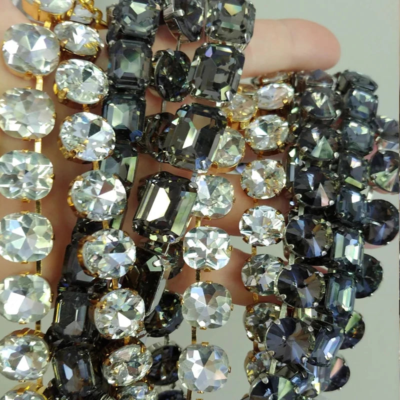 A close-up of a hand holding multiple strands of faceted rhinestone beads in black, dark gray, and clear crystal cuts with gold-toned settings.