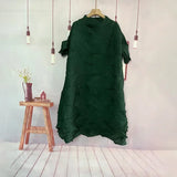 Green dress on a hanger against a white wall with a wooden stool and plant in the background.