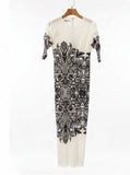 White dress with black pattern on a mannequin against a background of shelves with folded clothes.