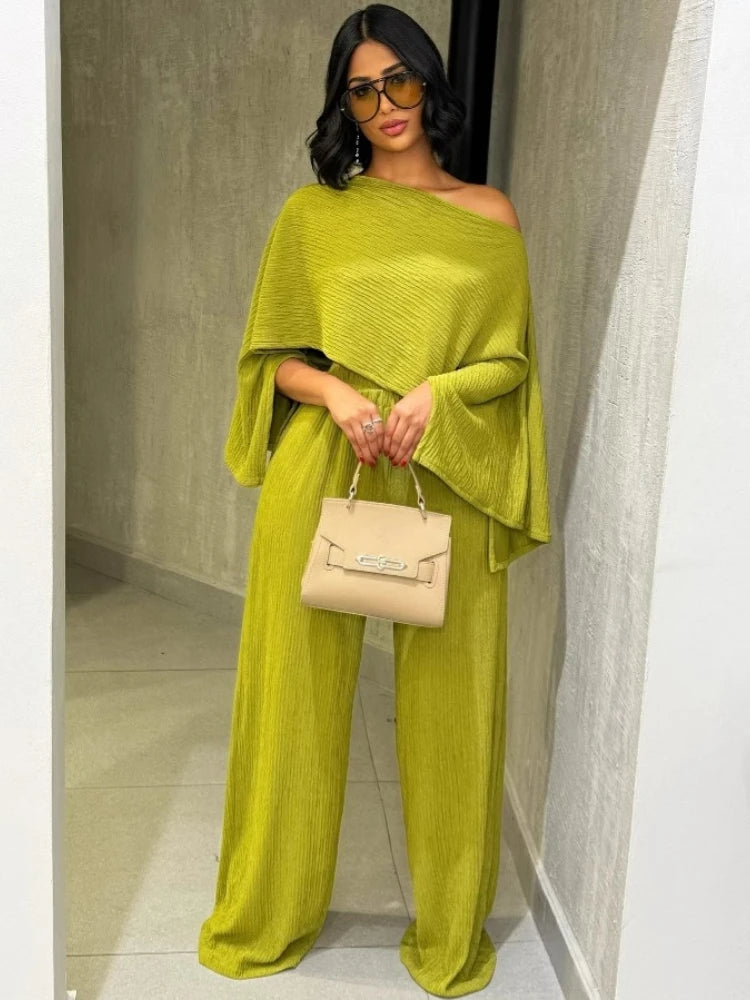 Woman in a green outfit holding a beige handbag indoors.