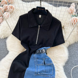 Black short-sleeve top with collar and zipper on a white fur surface, with blue jeans underneath.